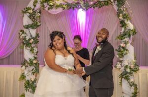Couple laughing with officiant Mylene Moraes under floral arch (Weddings by Mylene)